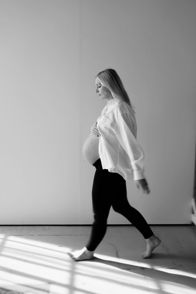 ann arbor photographer uses motion blur in this portrait of an expectant mother walking across a light studio with streaming light and shadows