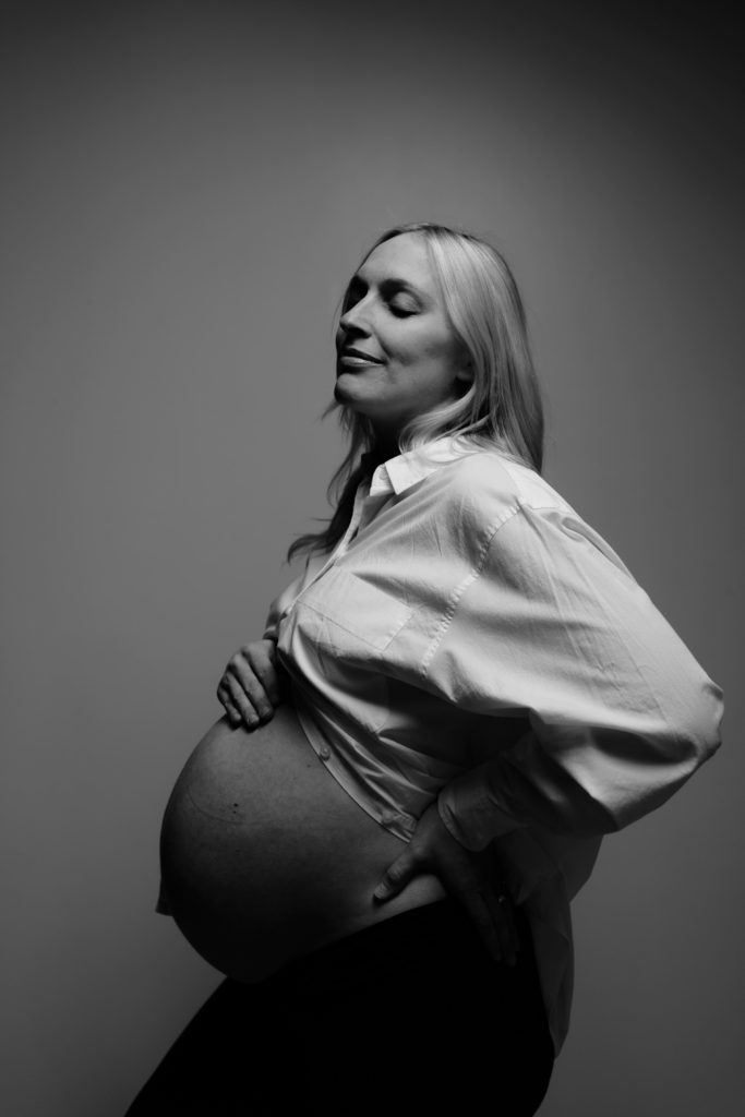 during this editorial maternity shoot and expecting mother smiles softly while resting a hand on her belly