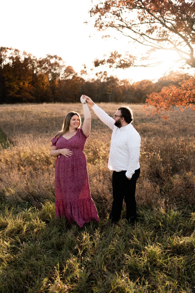 expecting couple dance in an open field during their luxury maternity photoshoot