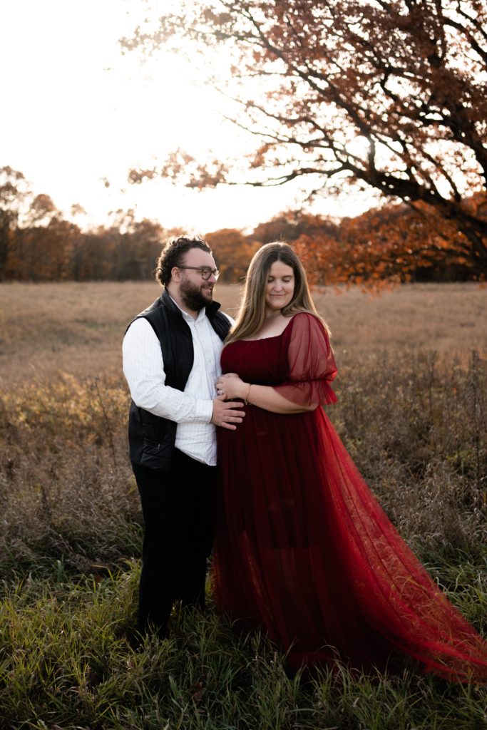 an expecting couple stand in front of an open michigan field during their luxury maternity photoshoot