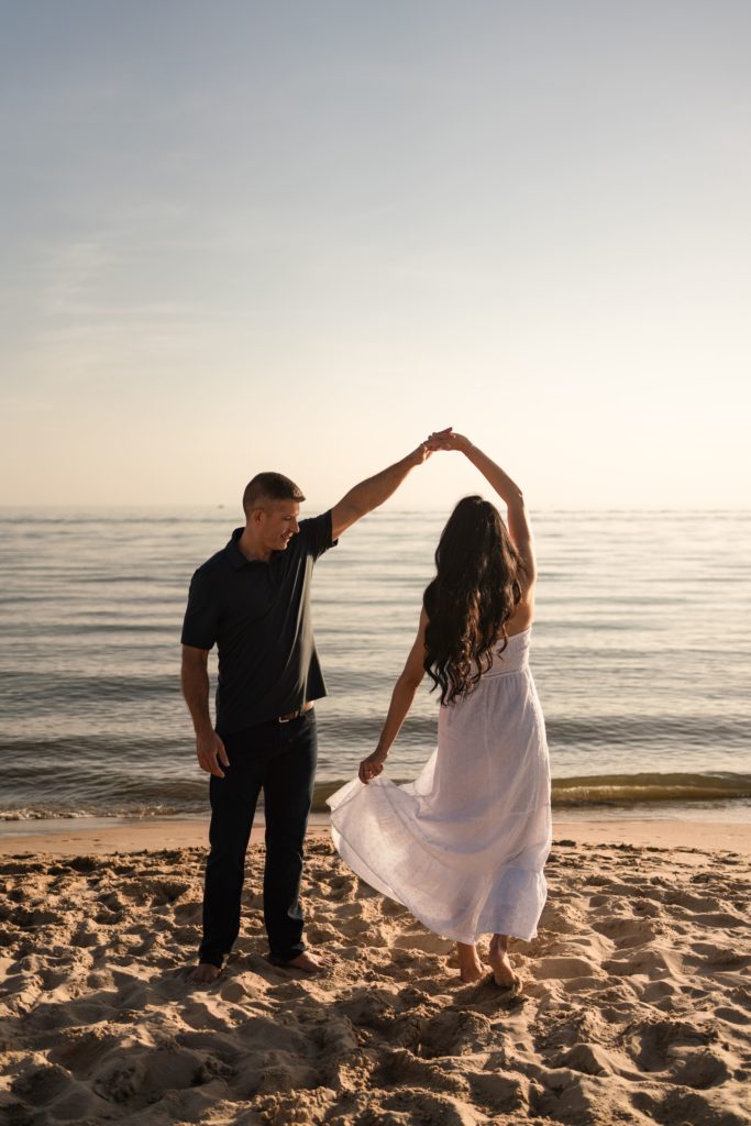 an engaged couple dance on the shore during their engagement photoshoot beach side