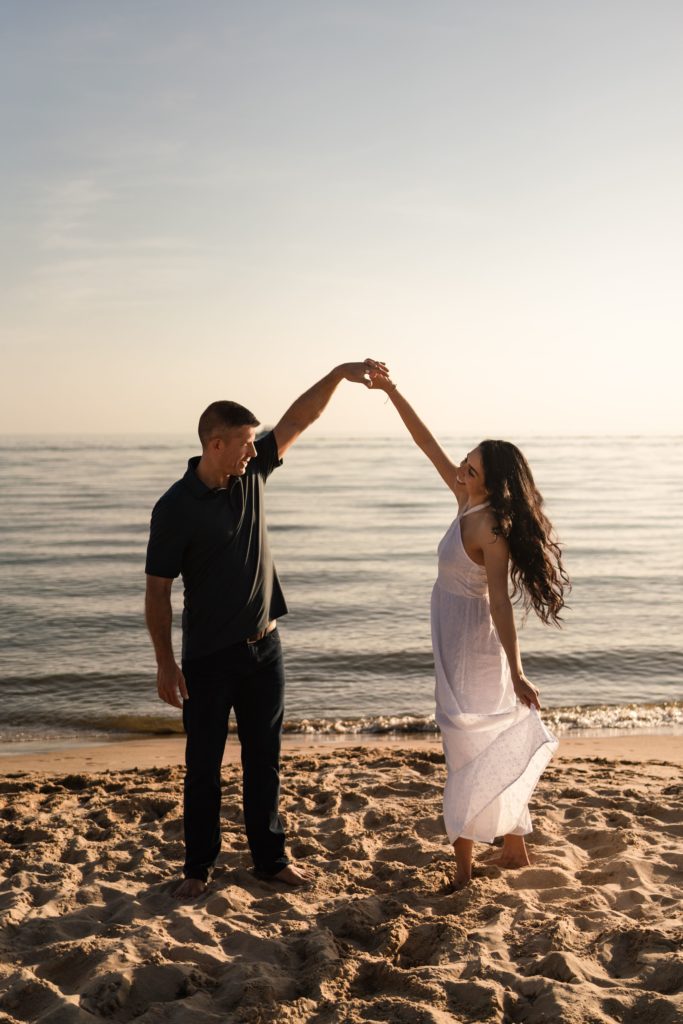 during an engagement photoshoot beach front, she beams over at him as they dance on the shore