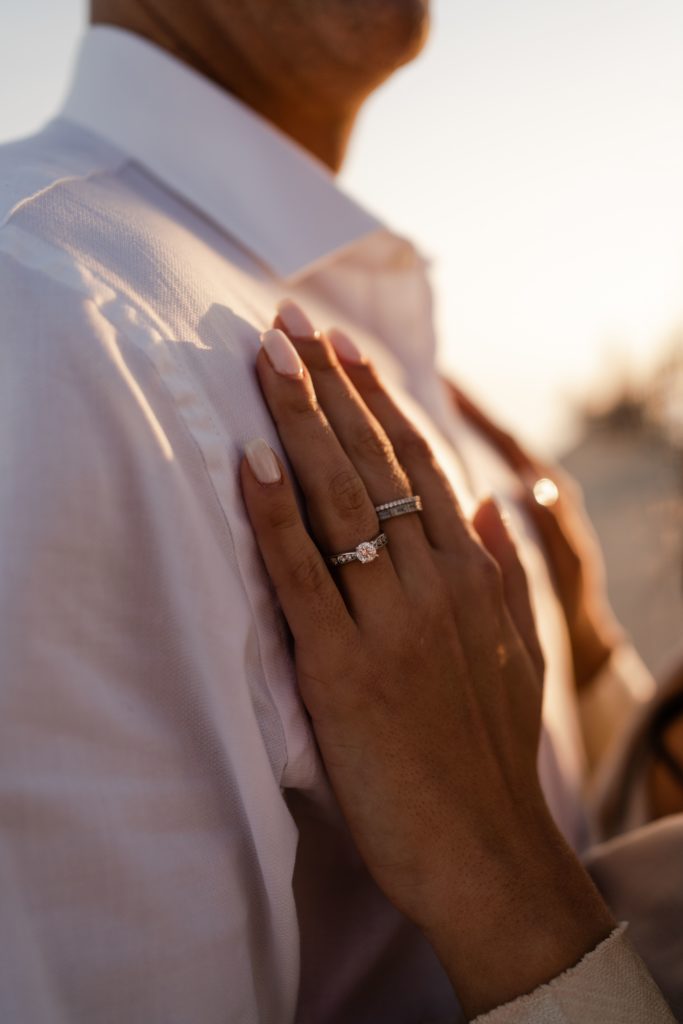 a woman rests her freshly manicured hands on her fiancees chest to show her engagement ring while michigan engagement photographer captures it
