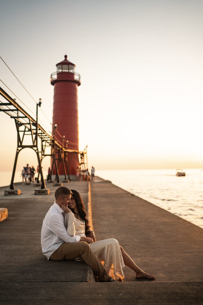 an engaged couple sit on the pier as grand haven photographers document their engagement