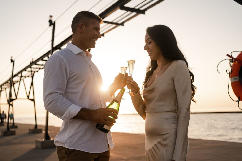 engaged couple toasts with champagne during michigan enagement photos on a pier
