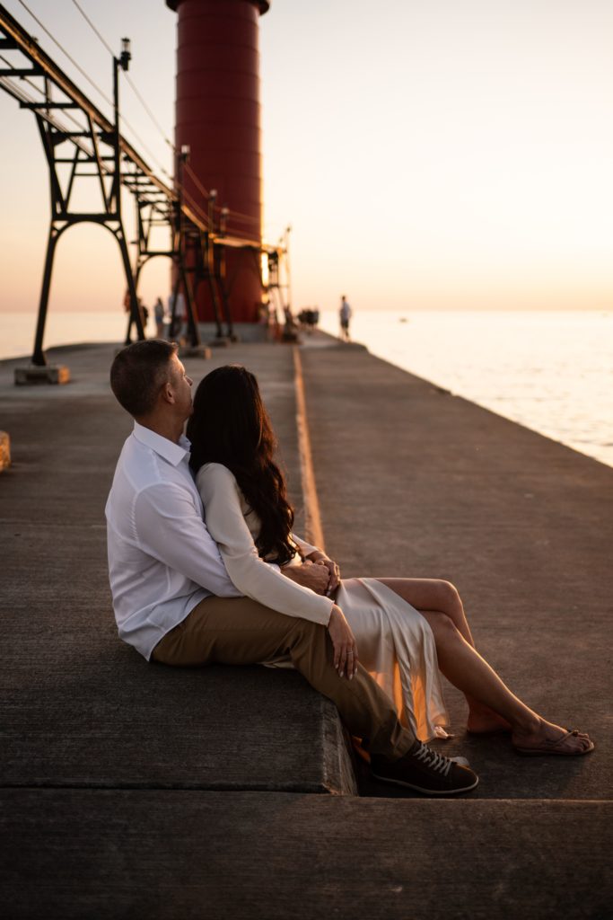 an engaged couple sit together on the pier as grand haven photographers document their engagement