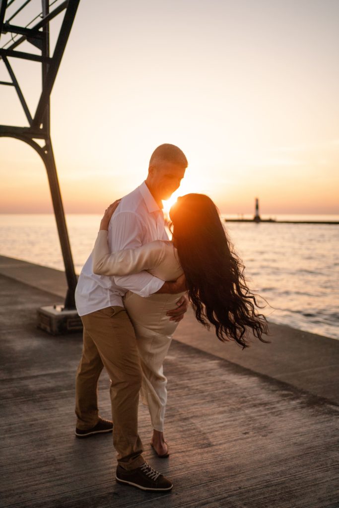 engaged couple gaze at each other as the sun sets behind them while he dips her while their michigan engagement photographer documents it
