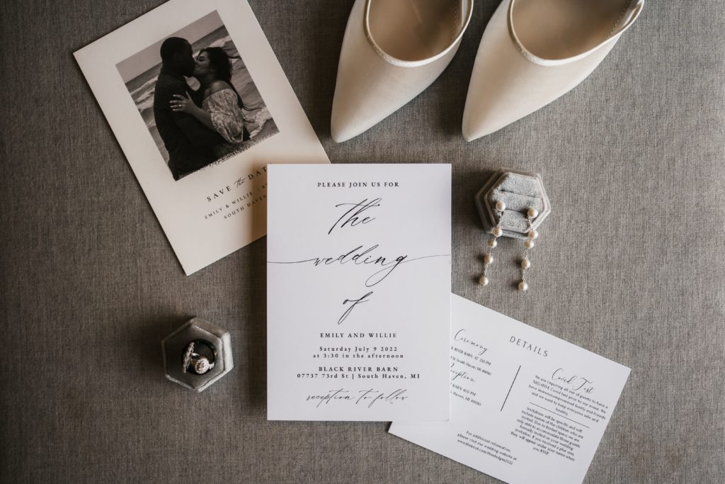 a detail shot of the wedding invitation suite featuring their save the date, the wedding invite, and detail insert sitting next to the bride's shoes, earrings, and the couple's rings shot by their luxury wedding photographer