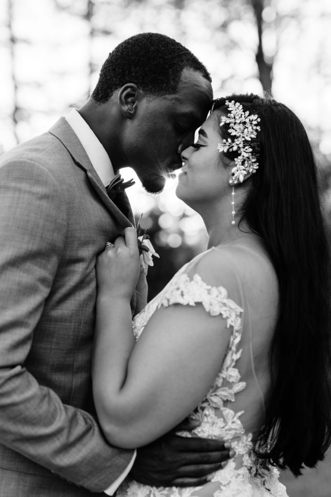 the bride and groom lean in for a kiss as the sun shines behind them. the bride holds on to the lapels of his suit jacket as he holds her natural waistline while they post for their luxury wedding photographer