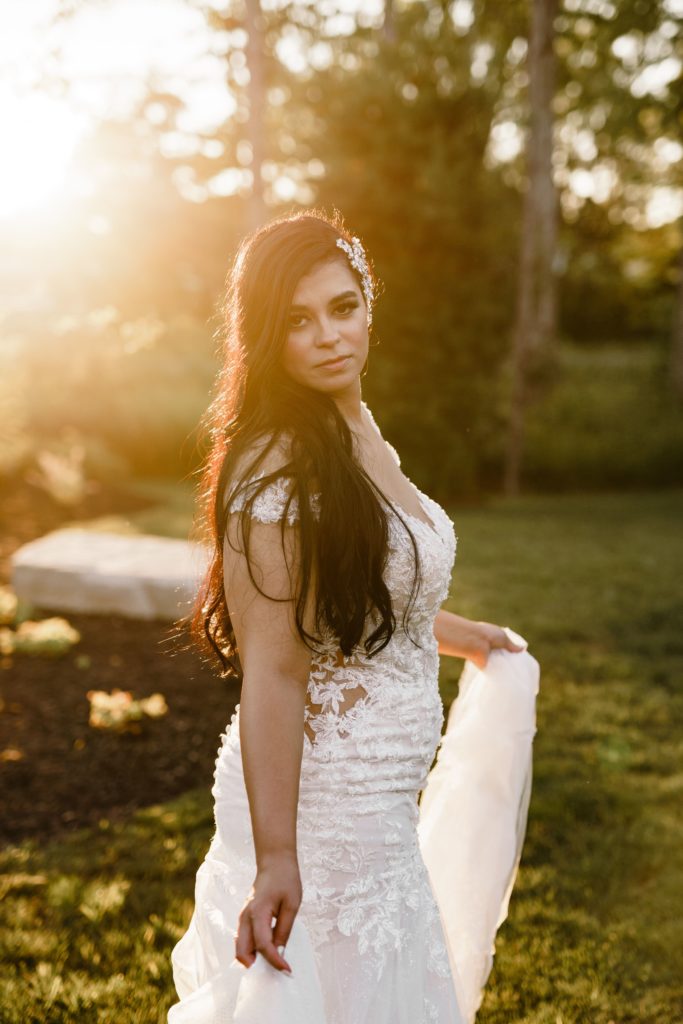 the bride holds her dress and gazes at the camera with golden light shining on her while posing for luxury wedding photography