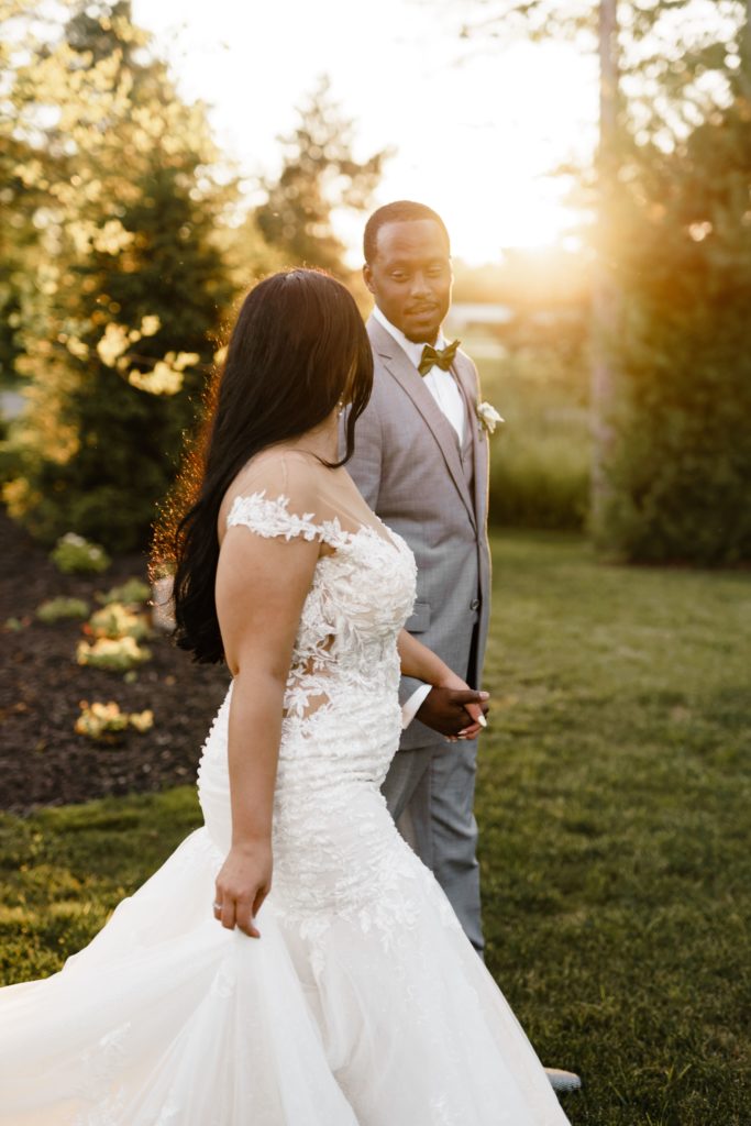 the bride and groom look at each other while holding hands as the golden sun shines from behind them while posing for their luxury wedding photographer