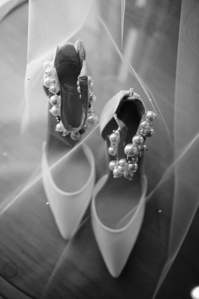 a photo of the bride's shoes standing under her veil in black and white taken by a luxury wedding photographer