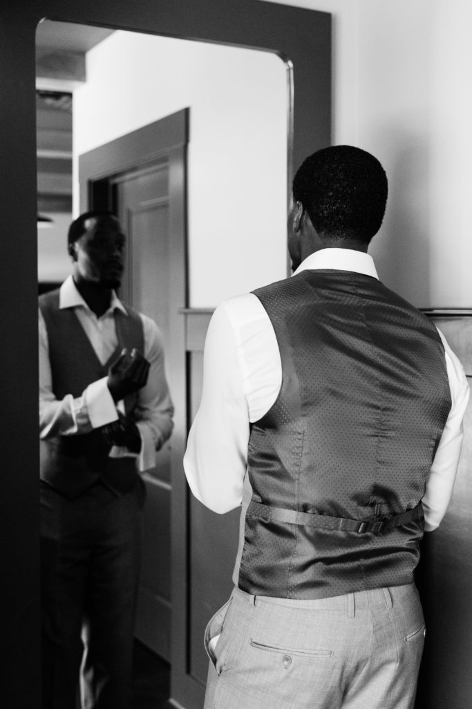 the groom checks himself in a mirror as he is getting ready for his south haven michigan wedding
