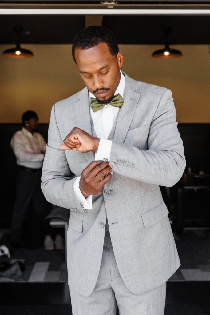 timeless wedding photography of the groom adjusting his cufflinks. he wears an olive green tie and a grey 3 piece suit