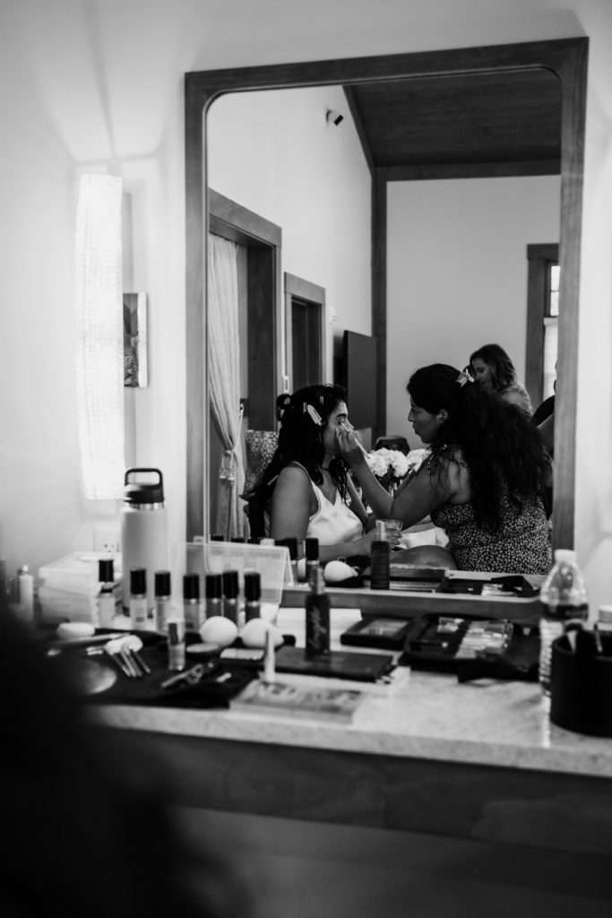the bride sits as her makeup is done for her wedding day while the michigan wedding photographer captures the reflection in the mirror