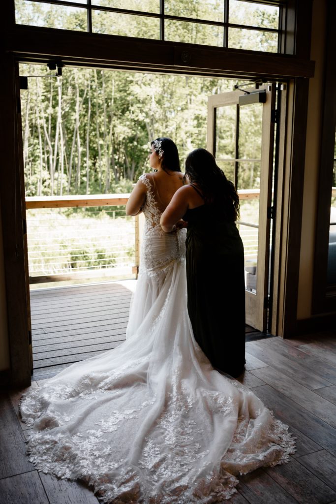the maid of honor helps the bride into her dress as they look off of the balcony at black river barn