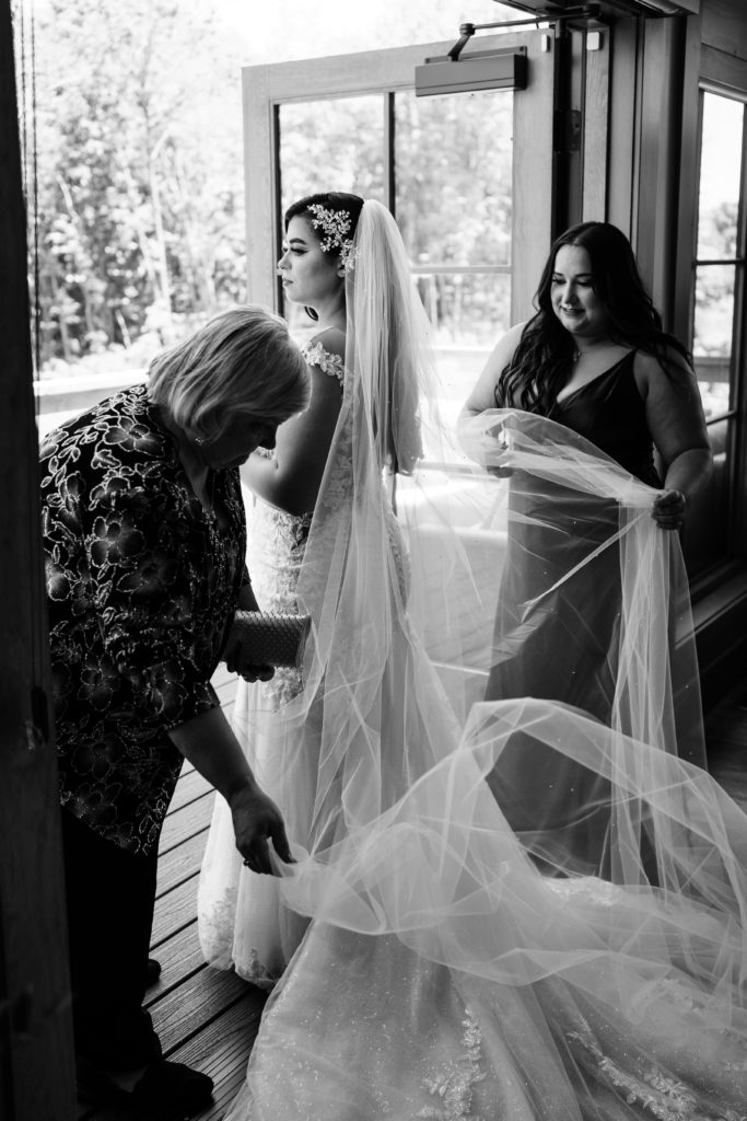 the maid of honor and the bride's mother adjust her veil as she is getting ready for her wedding day as it is documented with luxury wedding photography