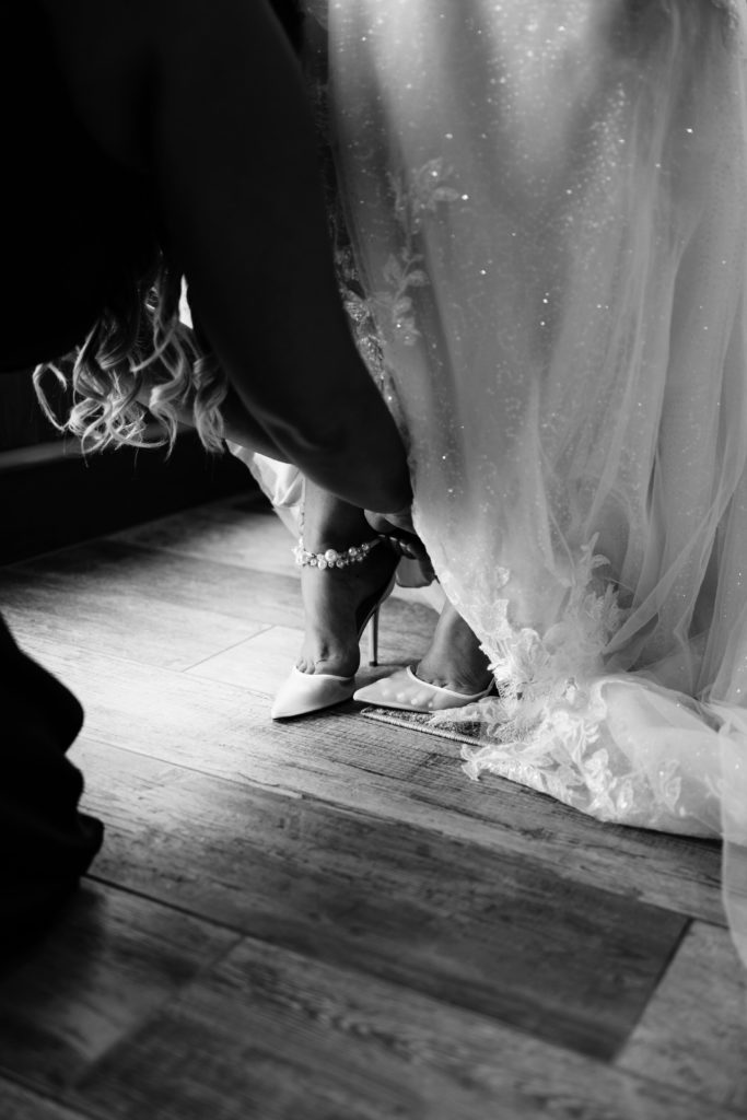 a bridesmaid helps the bride into her high heels as her michigan wedding photographer captures the getting ready process
