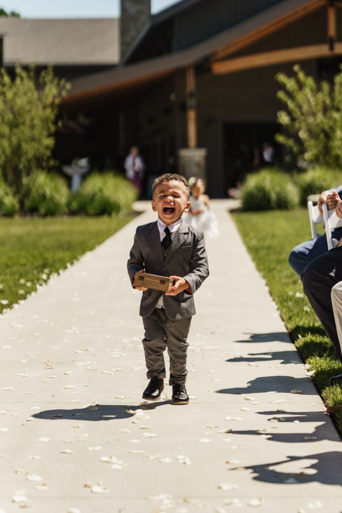the ring bearer makes a silly face at the luxury wedding photographer as he walks down the aisle