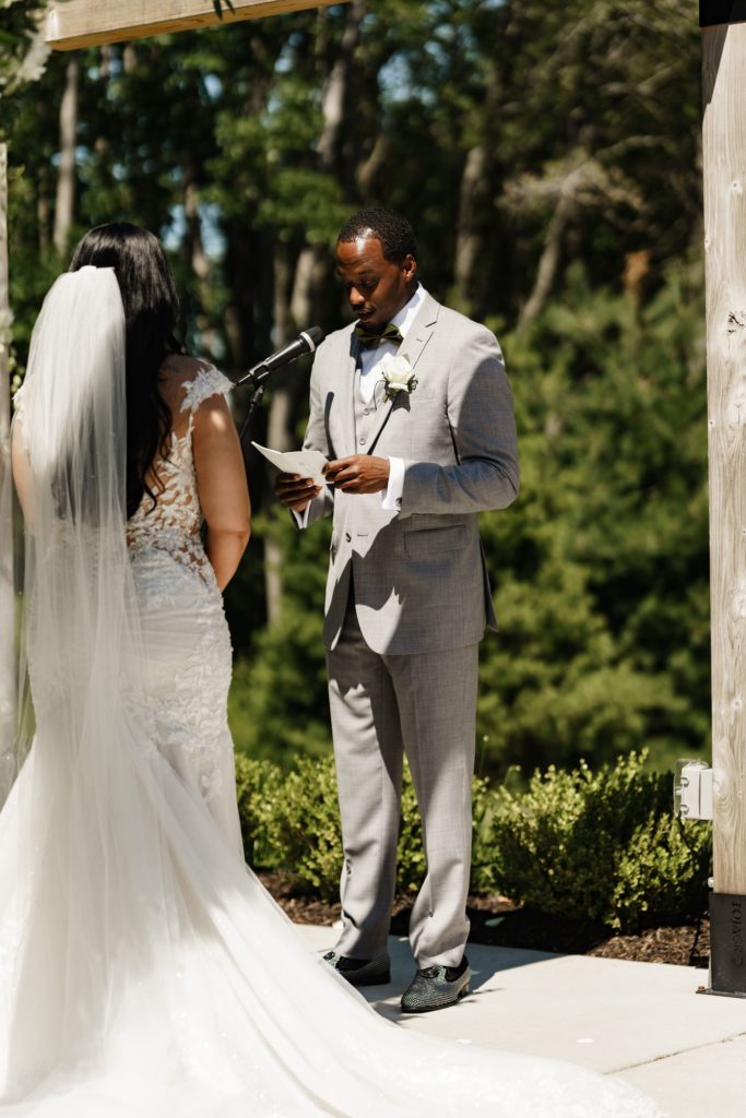 the bride stands facing the groom as he shares his wedding vows during the ceremony as their michigan wedding photographer captures the emotions