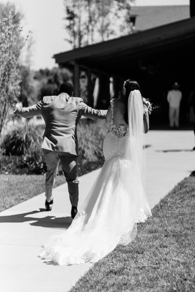 the groom dances happily holding hands with his new wife as they walk from the ceremony to the reception at their black river barn wedding