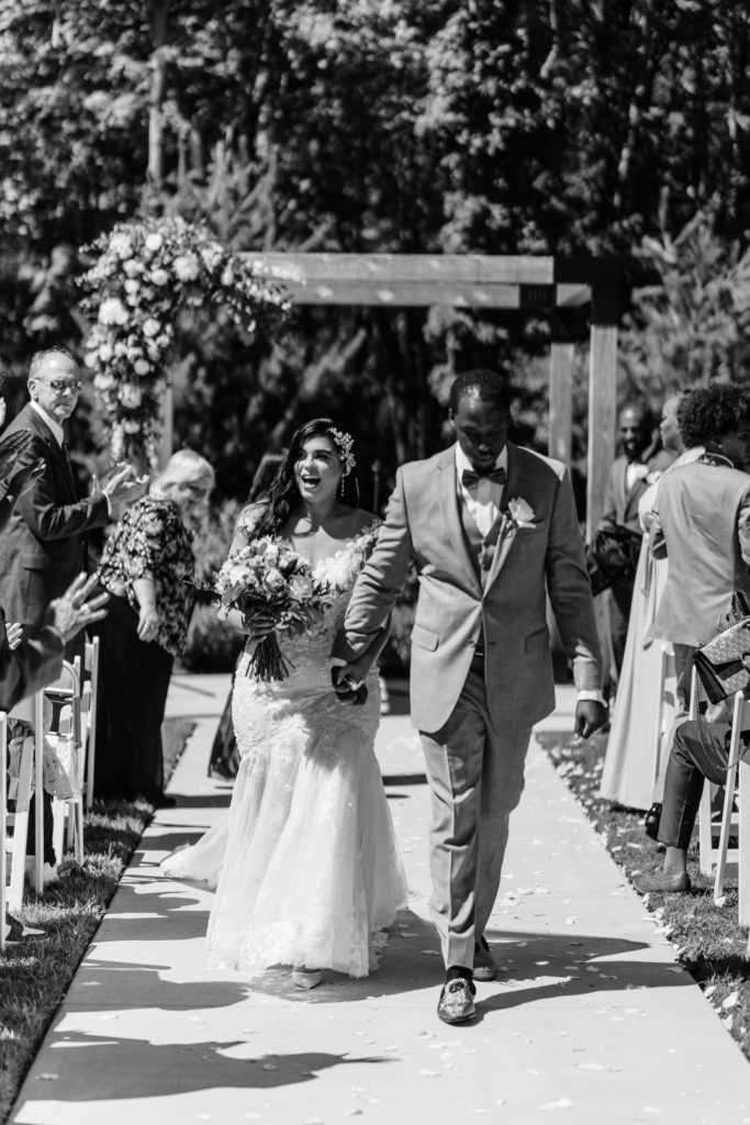 the bride and groom happily walk down the aisle together as their guests celebrate and their michigan wedding photographer captures the moment