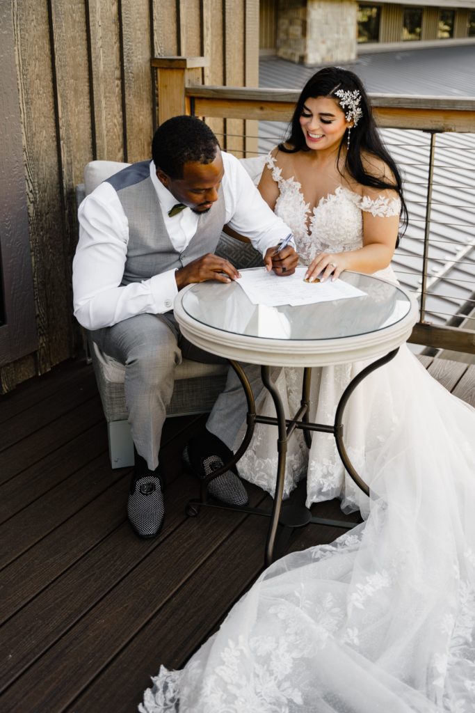 the bride beams as the groom signs their marriage certificate while their michigan wedding photographer captures the moment