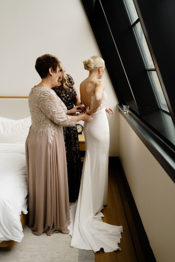the bride gets buttoned into her dress while being captured with luxury wedding photography