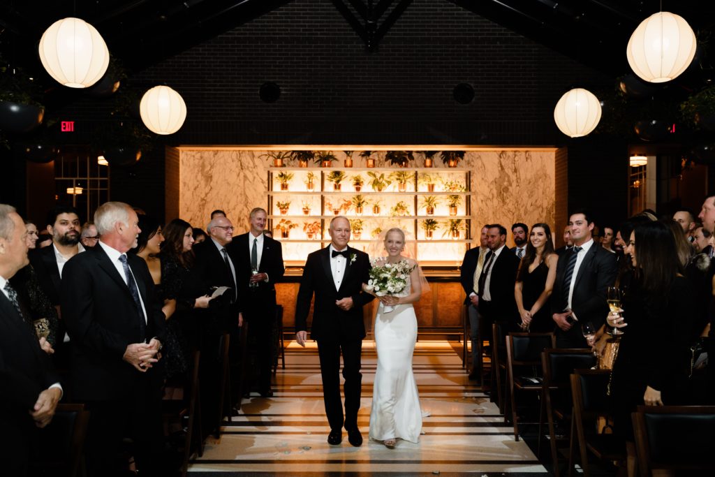 the bride walks down the aisle with her father at her shinola hotel wedding