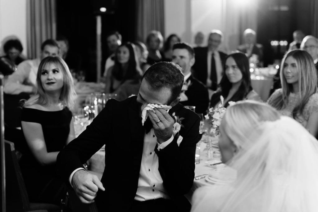 the groom wipes his tears while listening to speeches captured by a detroit wedding photographer