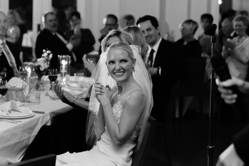 the bride smiles while listening to speeches captured by metro detroit wedding photographers