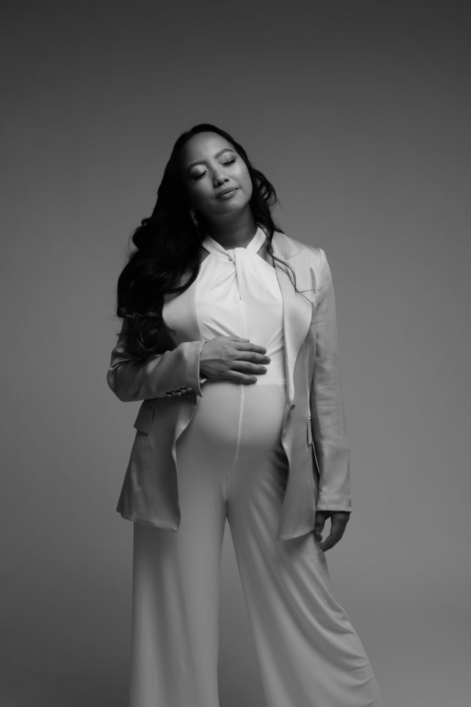 an expectant mother stands with her eyes closed and a hand resting on her belly during her luxury maternity photoshoot