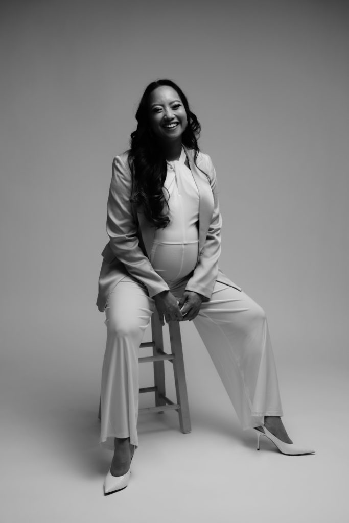 an expecting mother sits on a stool while smiling during her editorial maternity shoot