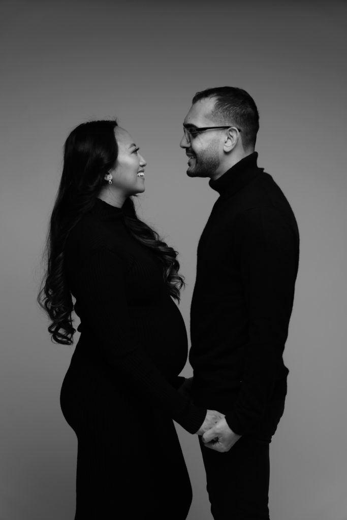 an expectant couple stand facing each other and smiling while posing for michigan maternity photographer