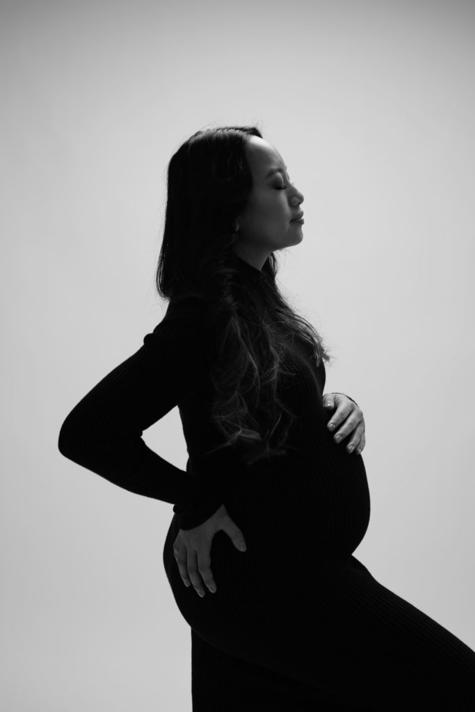 an expecting mother stands in dramatic lighting during her luxury maternity photoshoot
