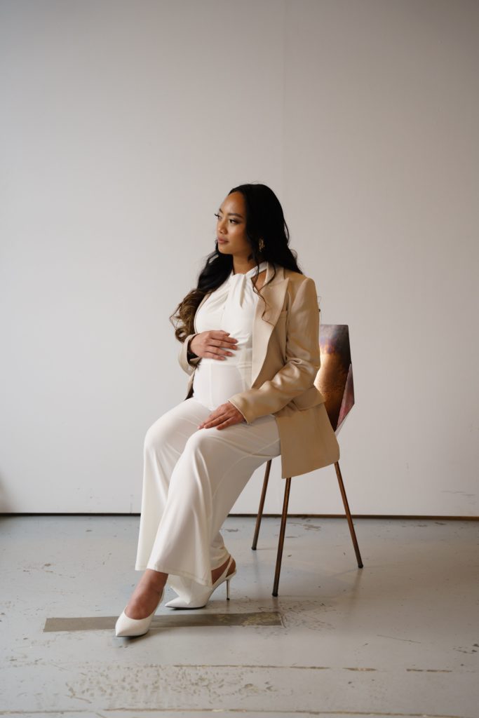 an expecting mother rests on a chair with a hand on her belly during her luxury maternity photoshoot