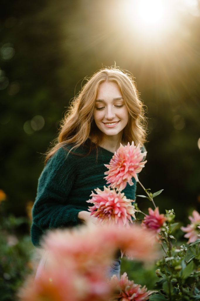 louise looks down at a flower as the sun shines behind her for her senior pictures michigan