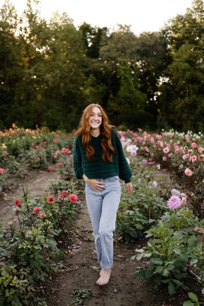 louise laughs while walking barefoot in a field of flowers for her senior portrait photography