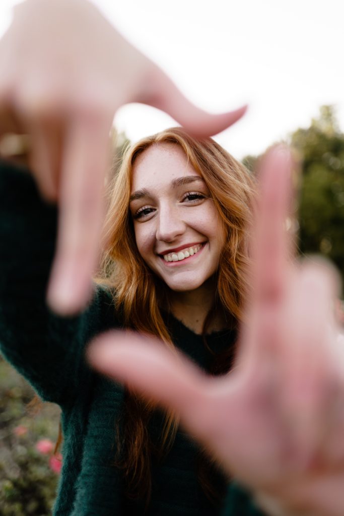 louise smiles as she holds her fingers out in the foreground for her senior portrait photography