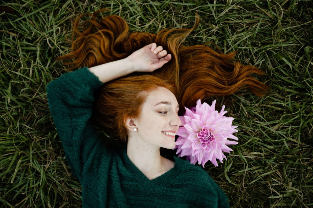 louise smiles over at a flower while sprawled out in the grass for her senior pictures detroit