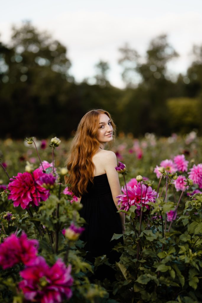 louise looks over her shoulder while standing in a field of flowers during her senior pictures detroit