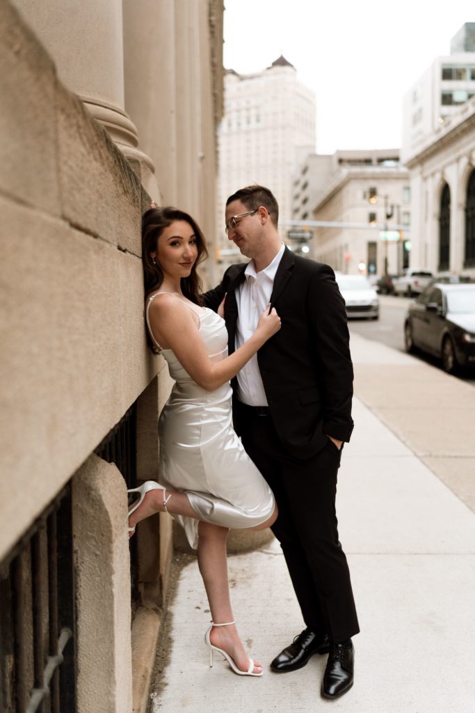 julia looks over at their engagement photographer as she stands against a wall with her fiancee