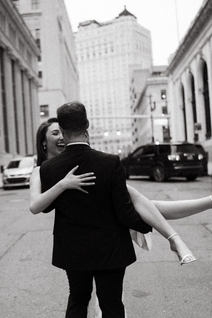 drew carries a laughing julia through the street in their downtown engagement photos