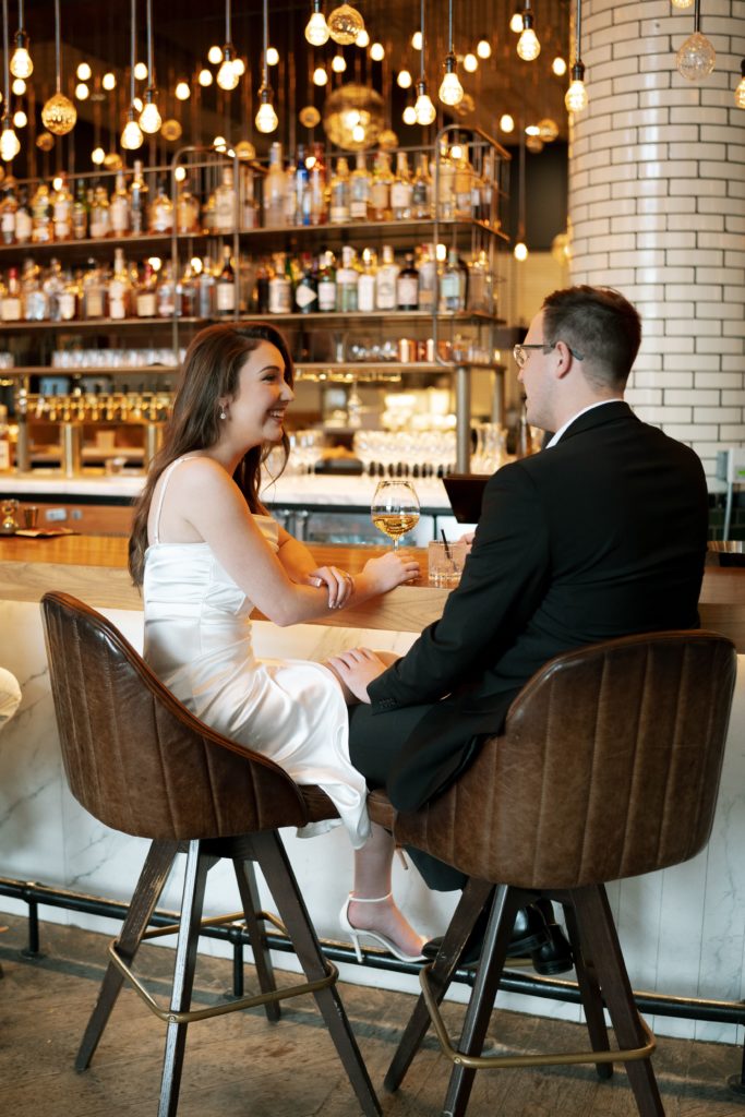 julia and drew sit at the bar at the apparatus room in downtown detroit in front of their engagement photographer