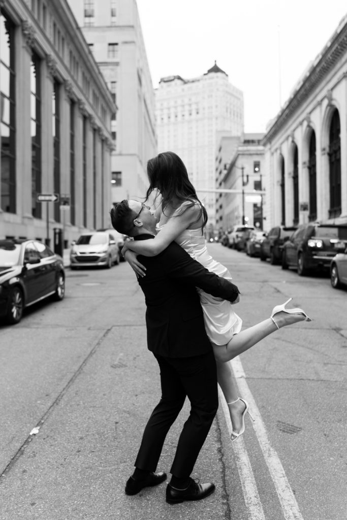 drew lifts julia in downtown detroit in front of their engagement photographer