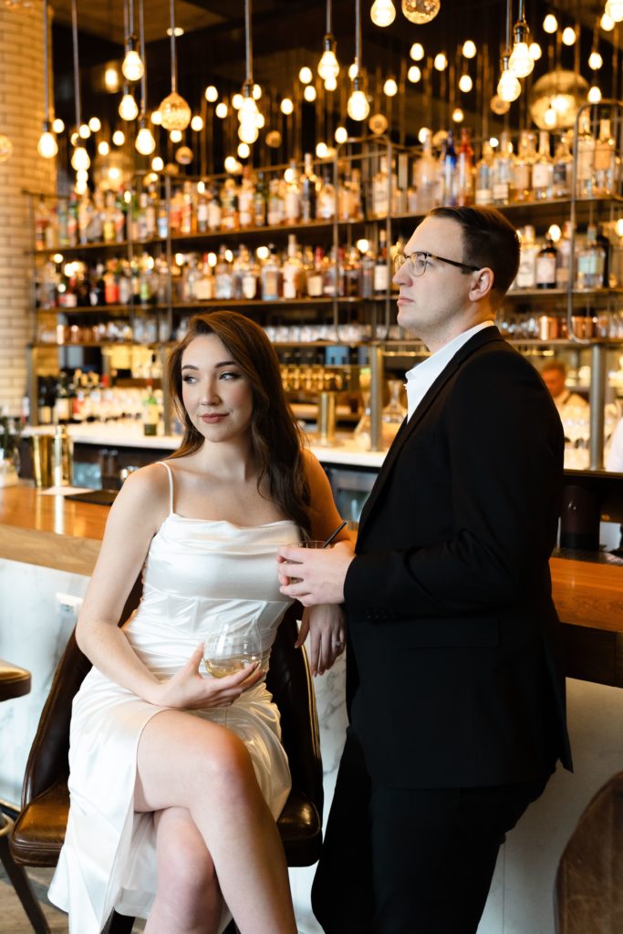 julia and drew look in different directions while sitting at the bar at the apparatus room during their engagement photoshoot