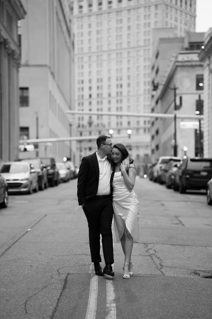 drew kisses his fiancee's forehead as they walk down the street during their detroit engagement photos