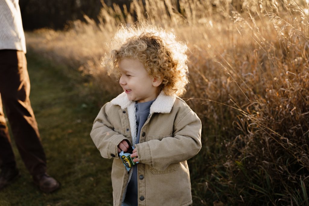 a boy with curly blonde hair smiles with joy while eating fruit snacks during a session with detroit family photographer