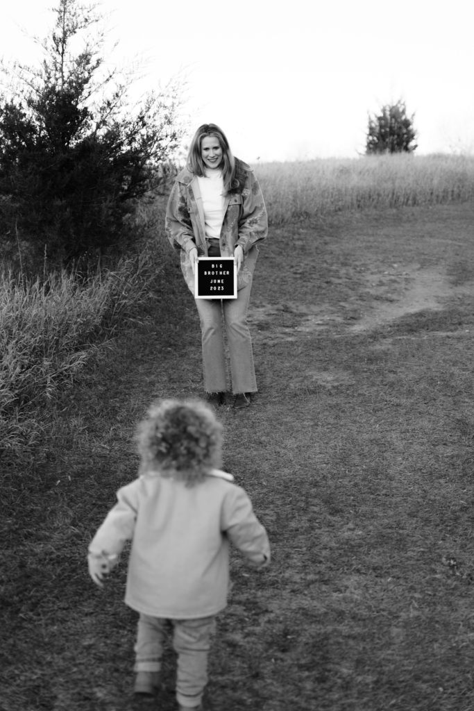 a boy runs towards his mom who is holding a letterboard that spells out "big brother" during a family portrait session