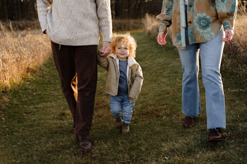 a little boy walks with his parents while holding his dad's hand during a session with a family photographer